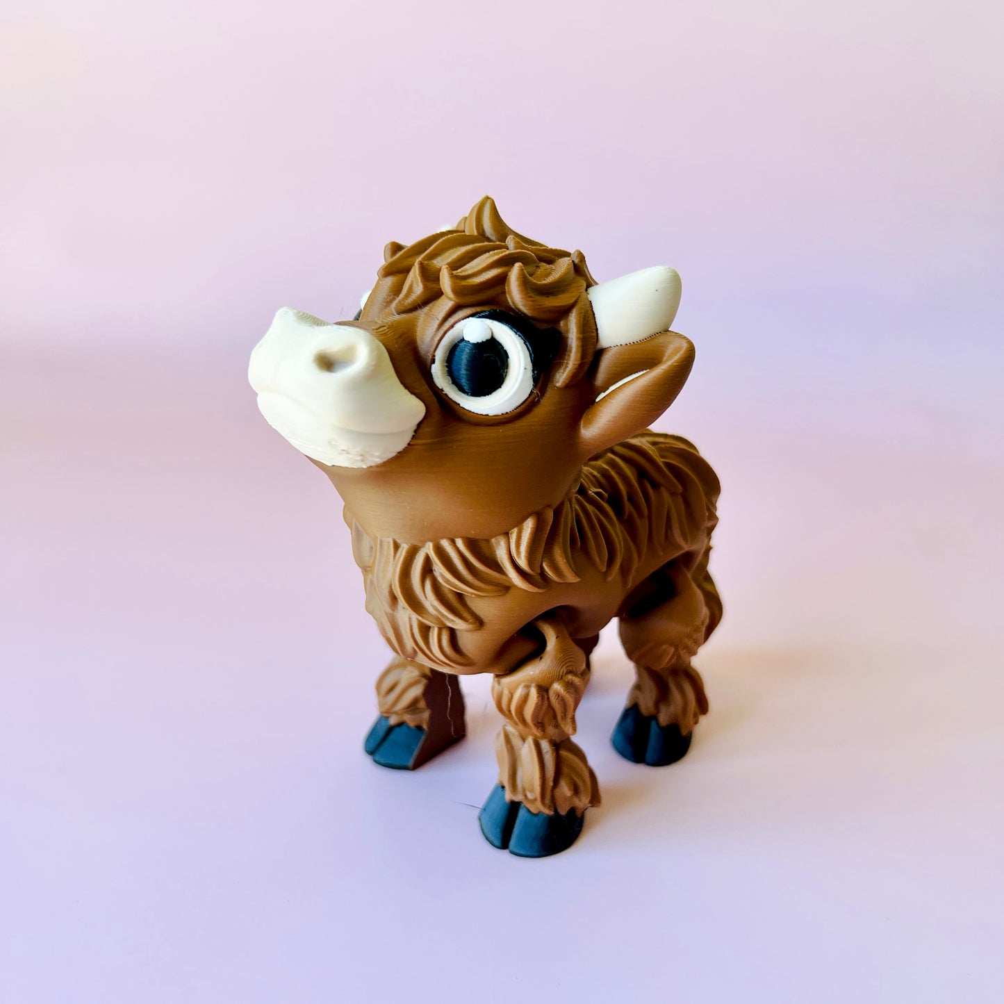 A cute Highland calf figurine with big eyes and curly fur, set against a soft pink background.