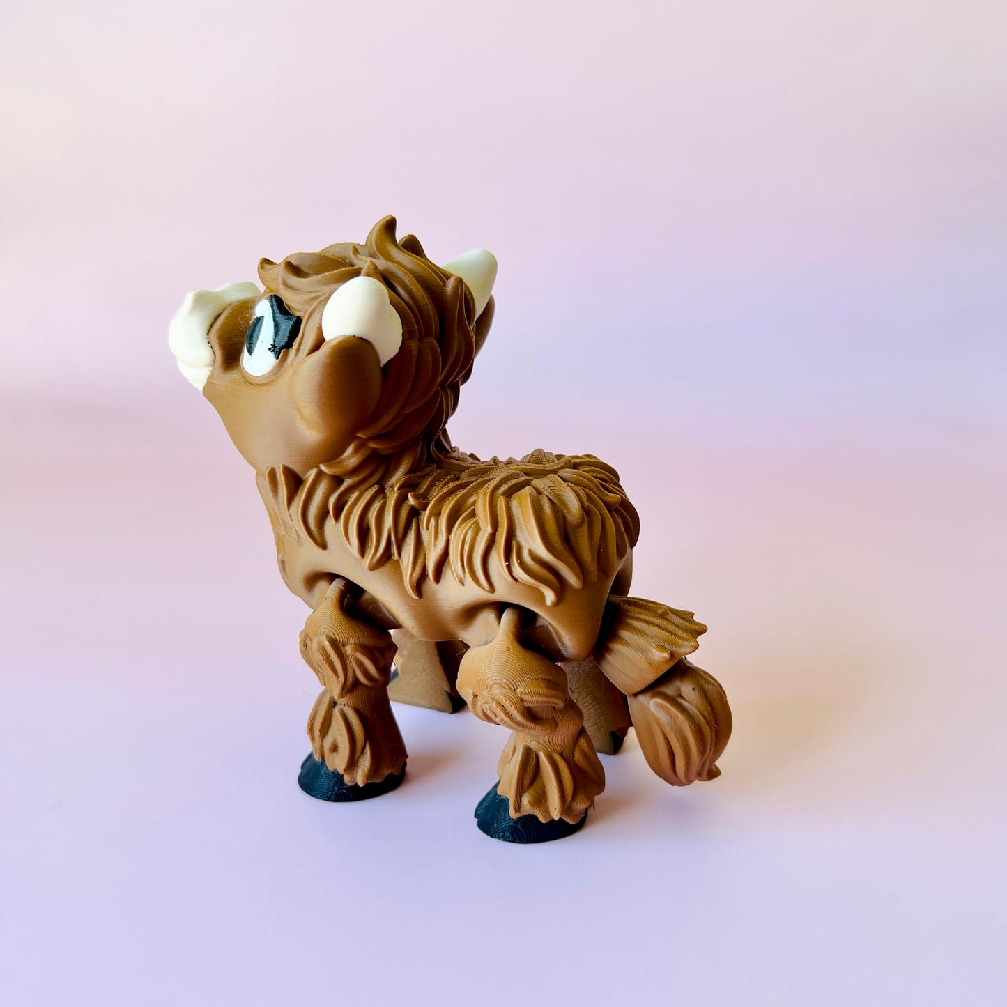 A whimsical brown Highland cow figure with textured fur and large white horns, set against a soft pink background.