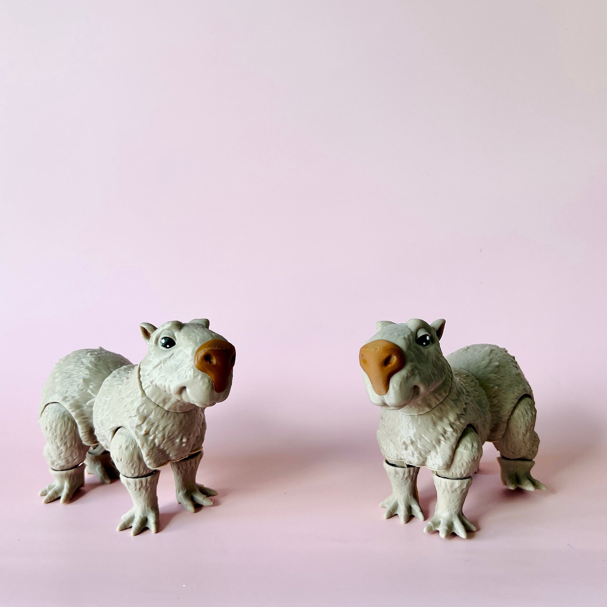 Two whimsical, gray creatures with round noses and expressive eyes stand against a soft pink background.