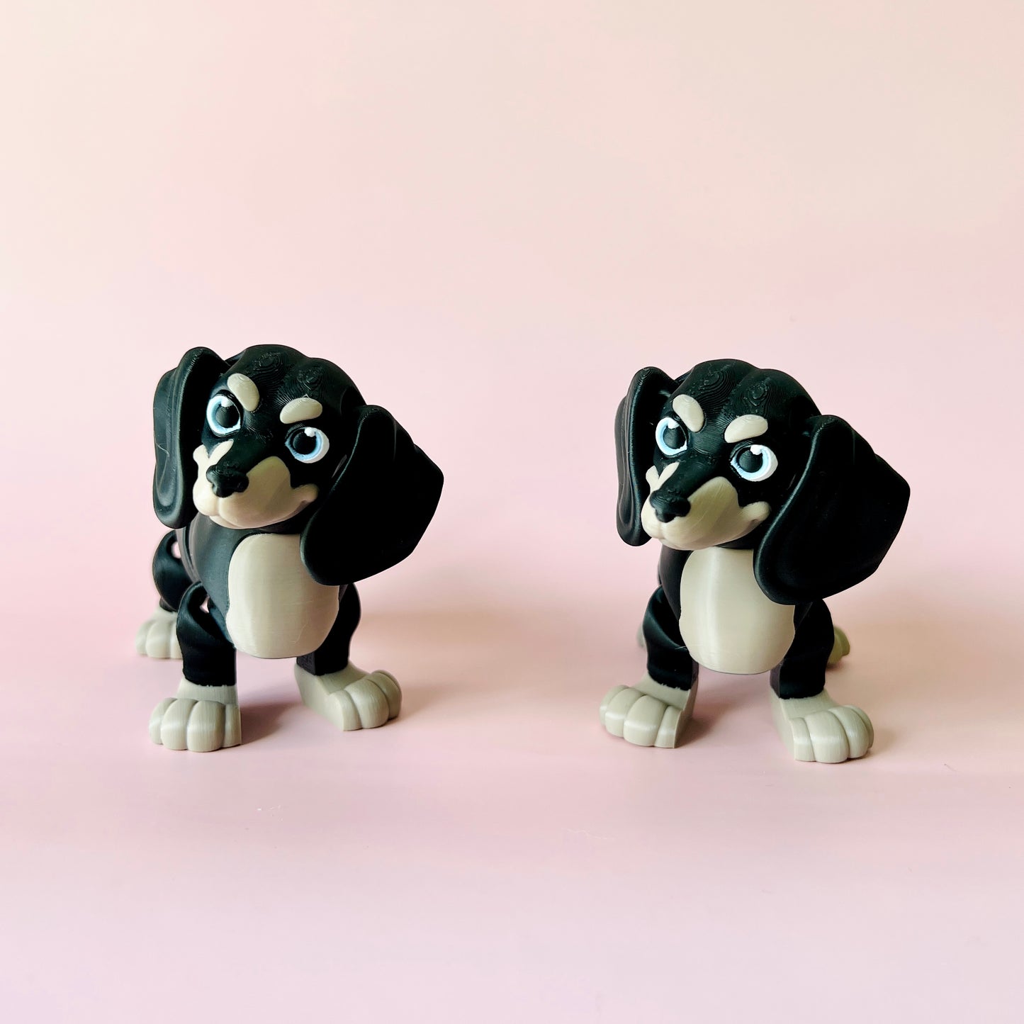 Two playful black and gray figurines resembling dogs, set against a soft pink background.