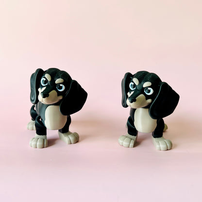 Two playful black and gray figurines resembling dogs, set against a soft pink background.