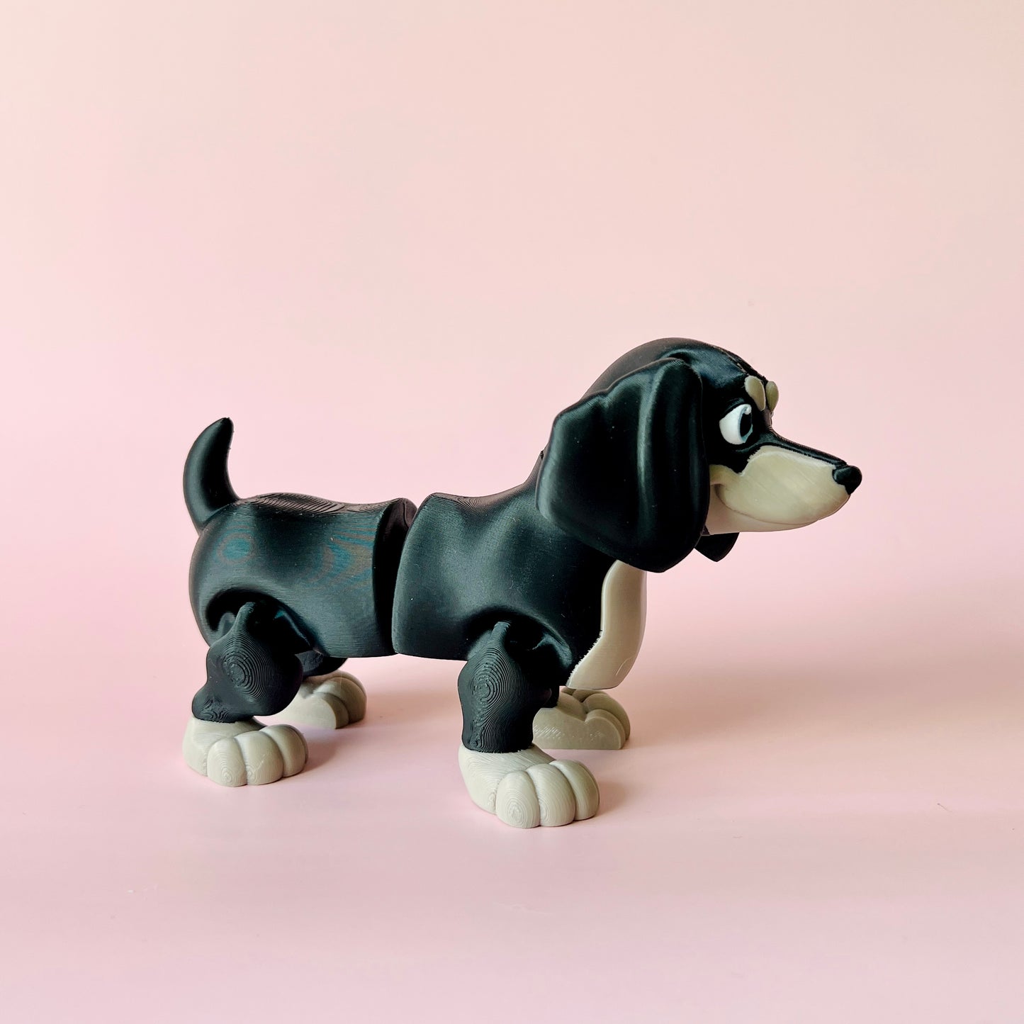 A playful black and white dog figure stands on a soft pink background, showcasing a charming, cartoonish design.