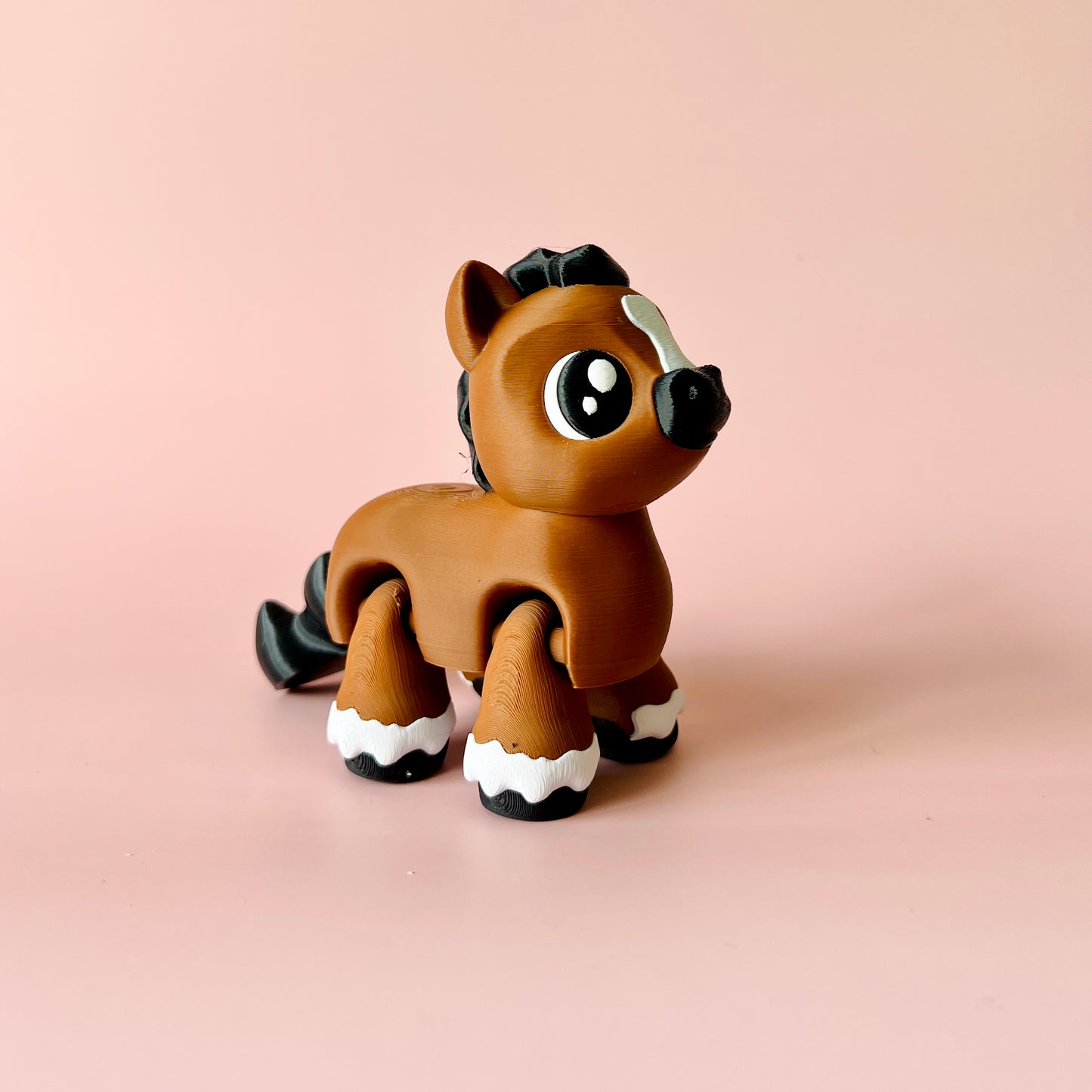 A cheerful brown horse figure with large eyes, a black mane, and white hoof accents on a soft pink background.
