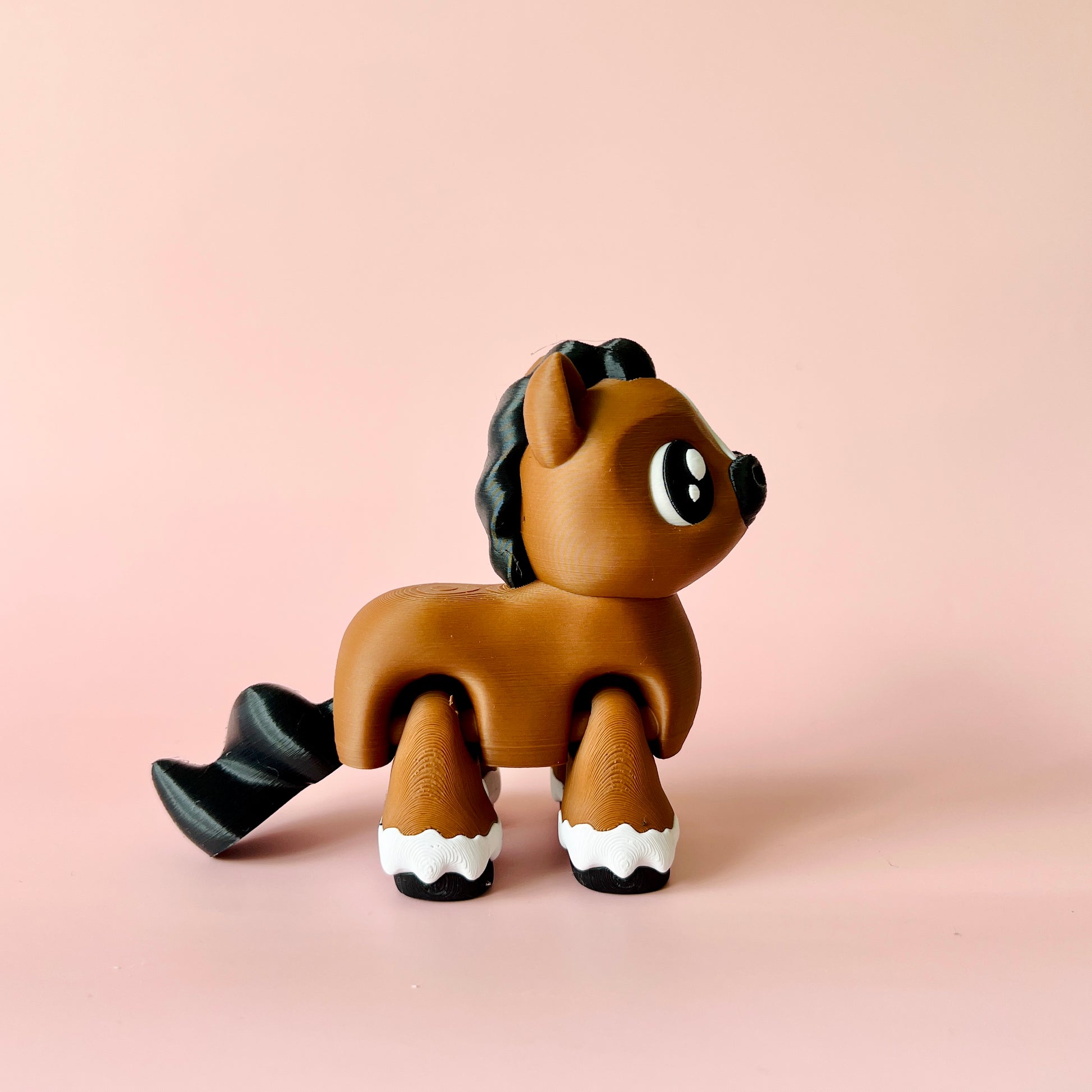 A cute brown figure with a black mane and tail, standing against a soft pink background, showcasing large expressive eyes.