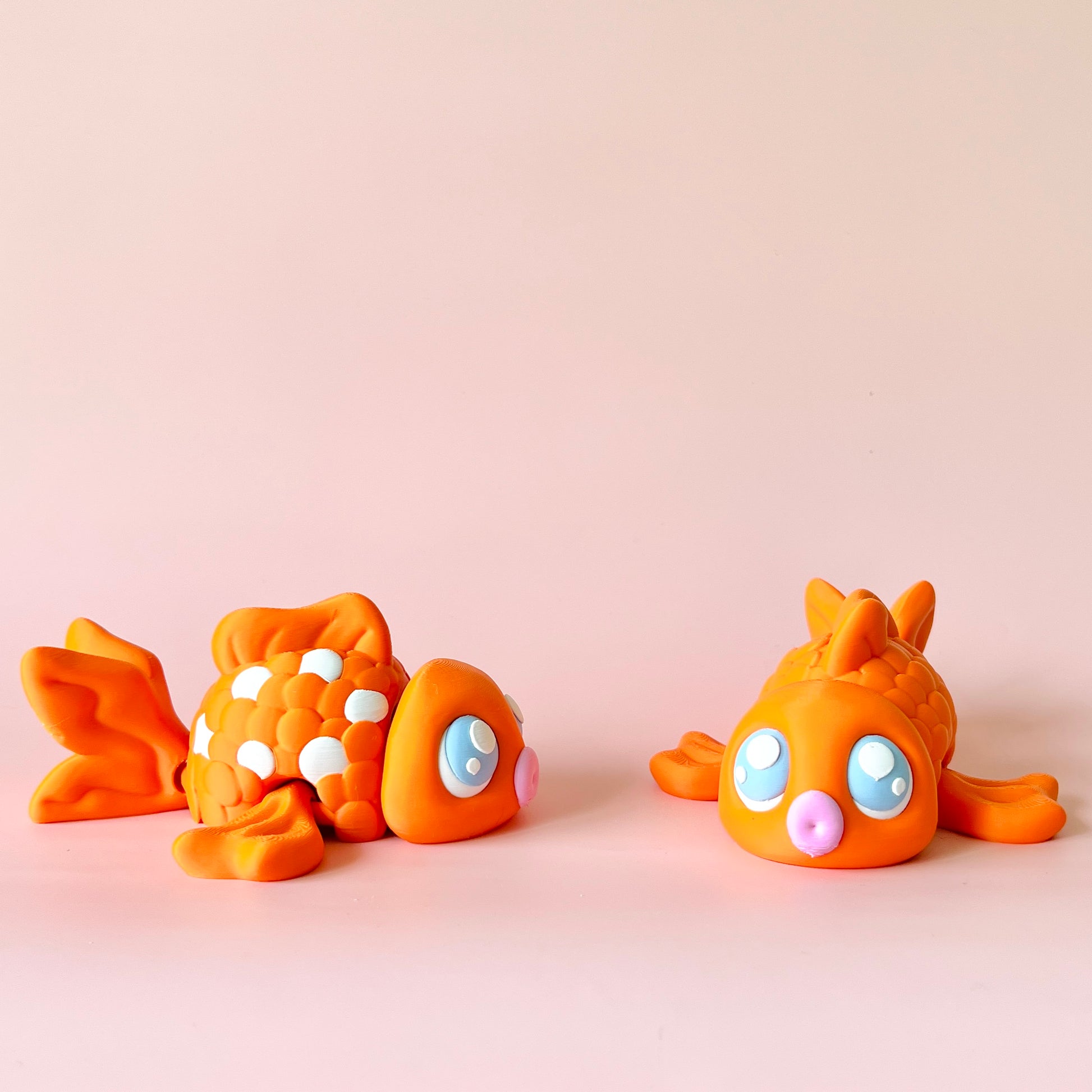 Two playful orange fish figures with bright blue eyes and pink accents on a soft pink background.