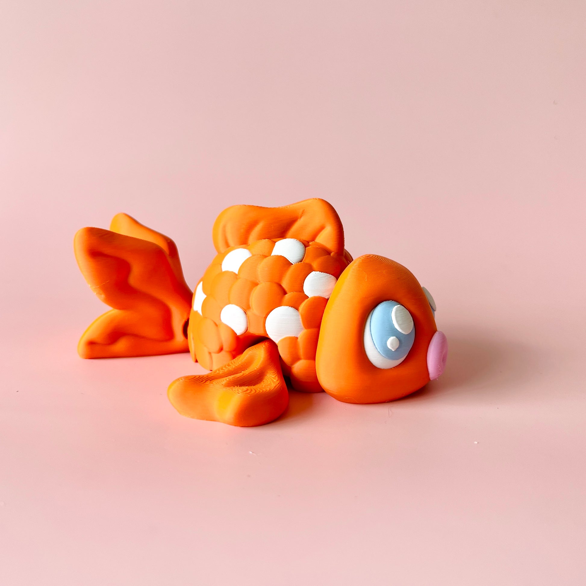 A vibrant orange fish with white spots, resting against a soft pink background, showcasing playful features.