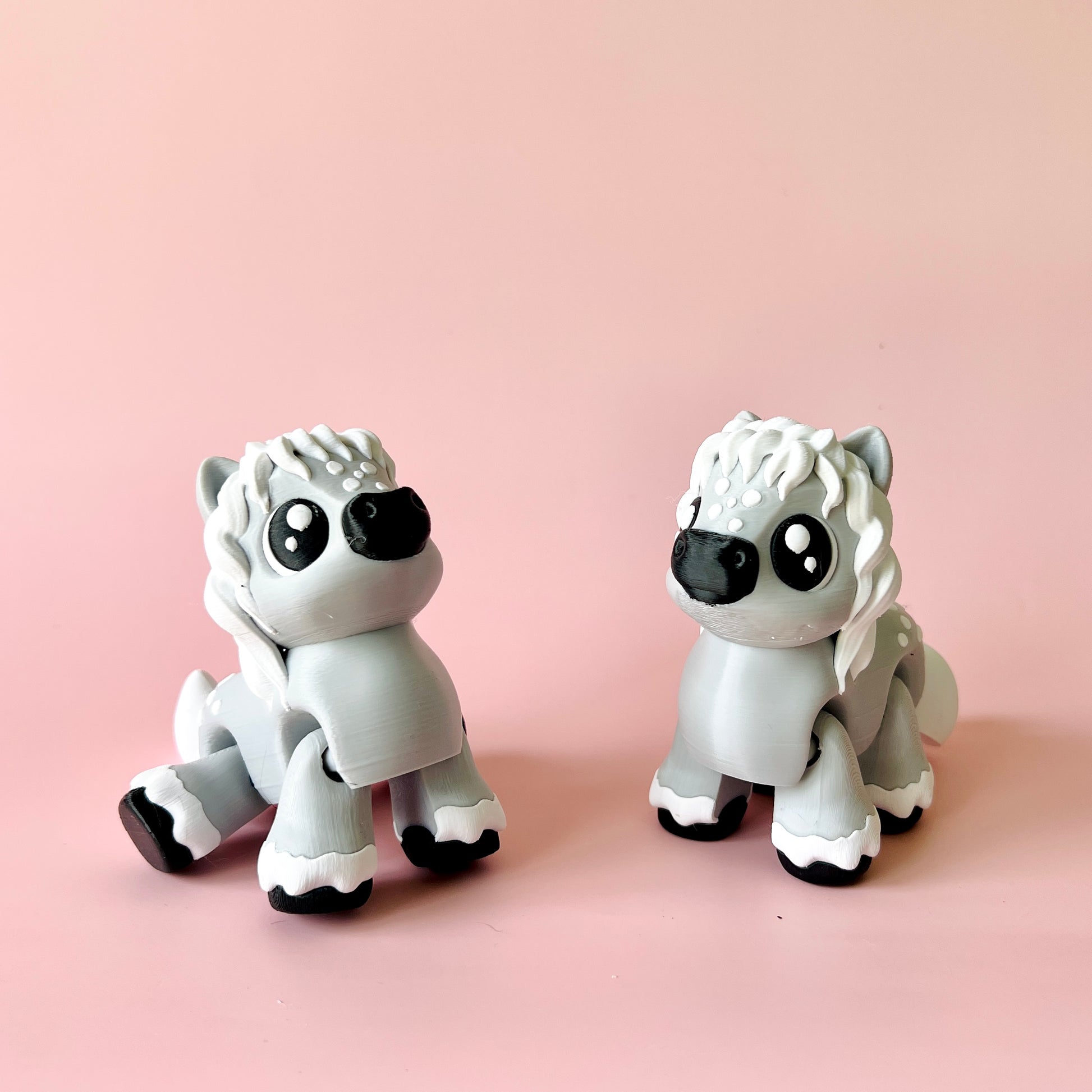 Two cute gray figurines resembling fluffy animals with large eyes, set against a soft pink background.