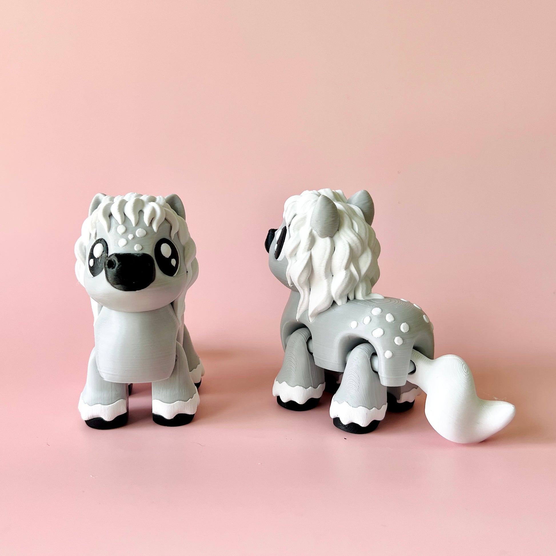 Two cute gray figures with fluffy manes and expressive eyes, set against a soft pink background.
