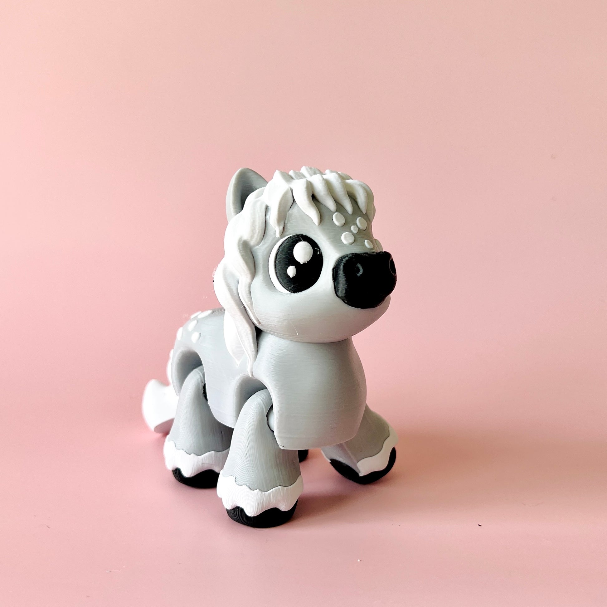 A cute, gray figurine with large eyes and a fluffy mane, set against a soft pink background.