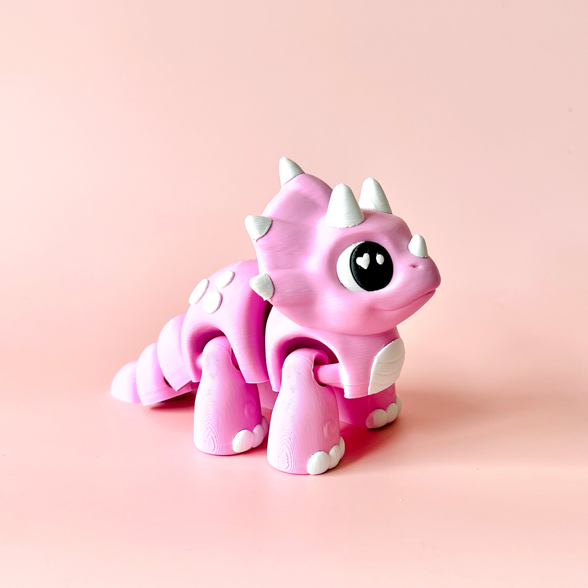 A cute, pink dinosaur figure with white spikes and big expressive eyes against a soft pink background.