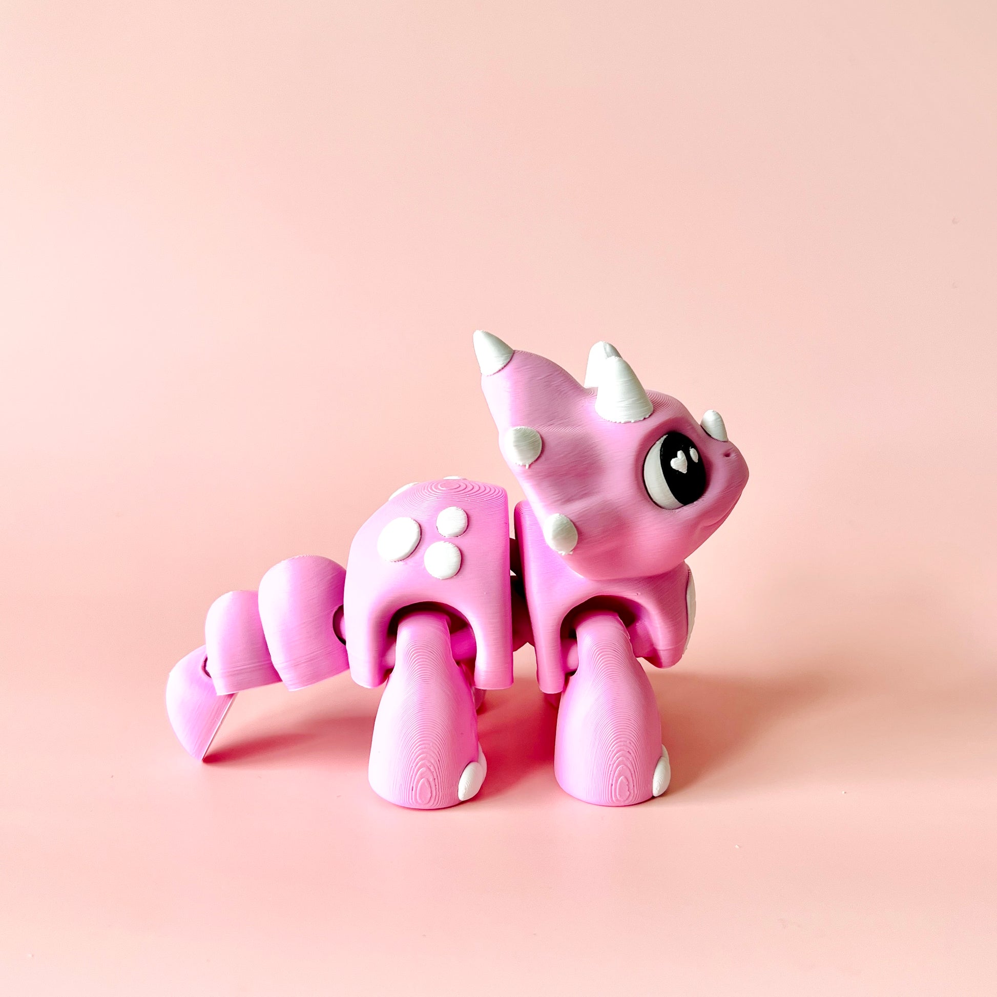 A cute pink creature with spikes and large eyes, set against a soft pink background.