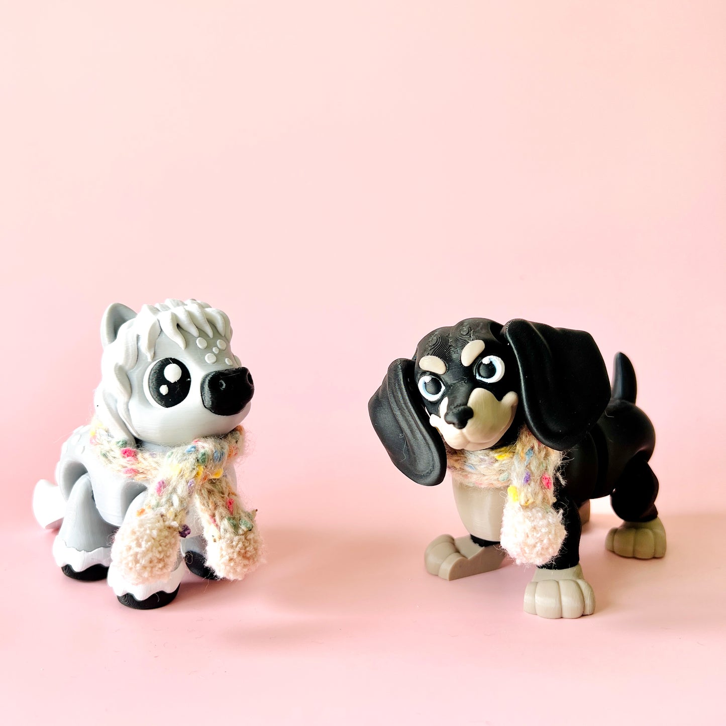 Two whimsical, colorful dog figures with scarves on a soft pink background.