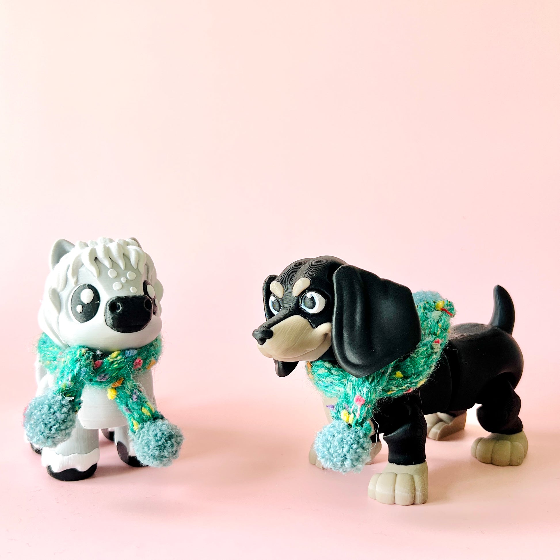 Two whimsical figures wearing colorful scarves stand against a soft pink background, showcasing playful expressions.