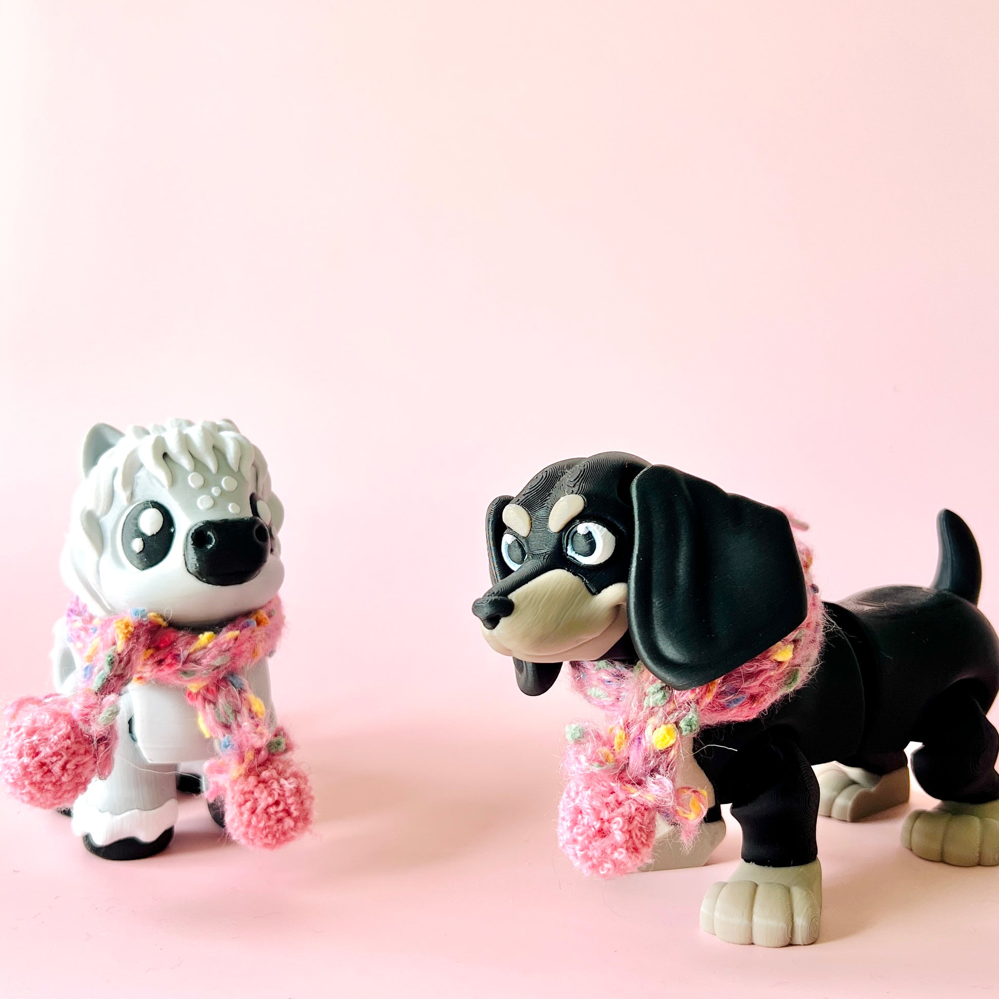 Two colorful dog figures wearing pink and multicolored scarves, set against a soft pink background.