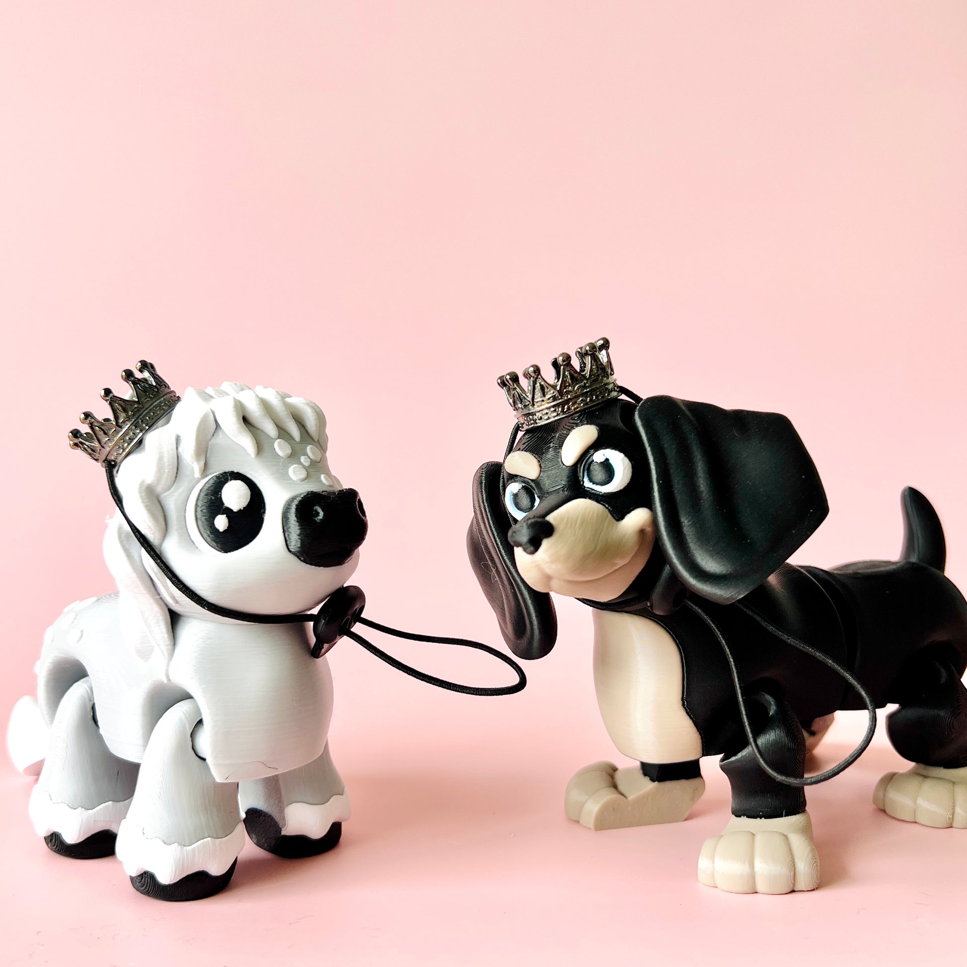 Two charming crowned figurines of a white and black dog, set against a soft pink background.