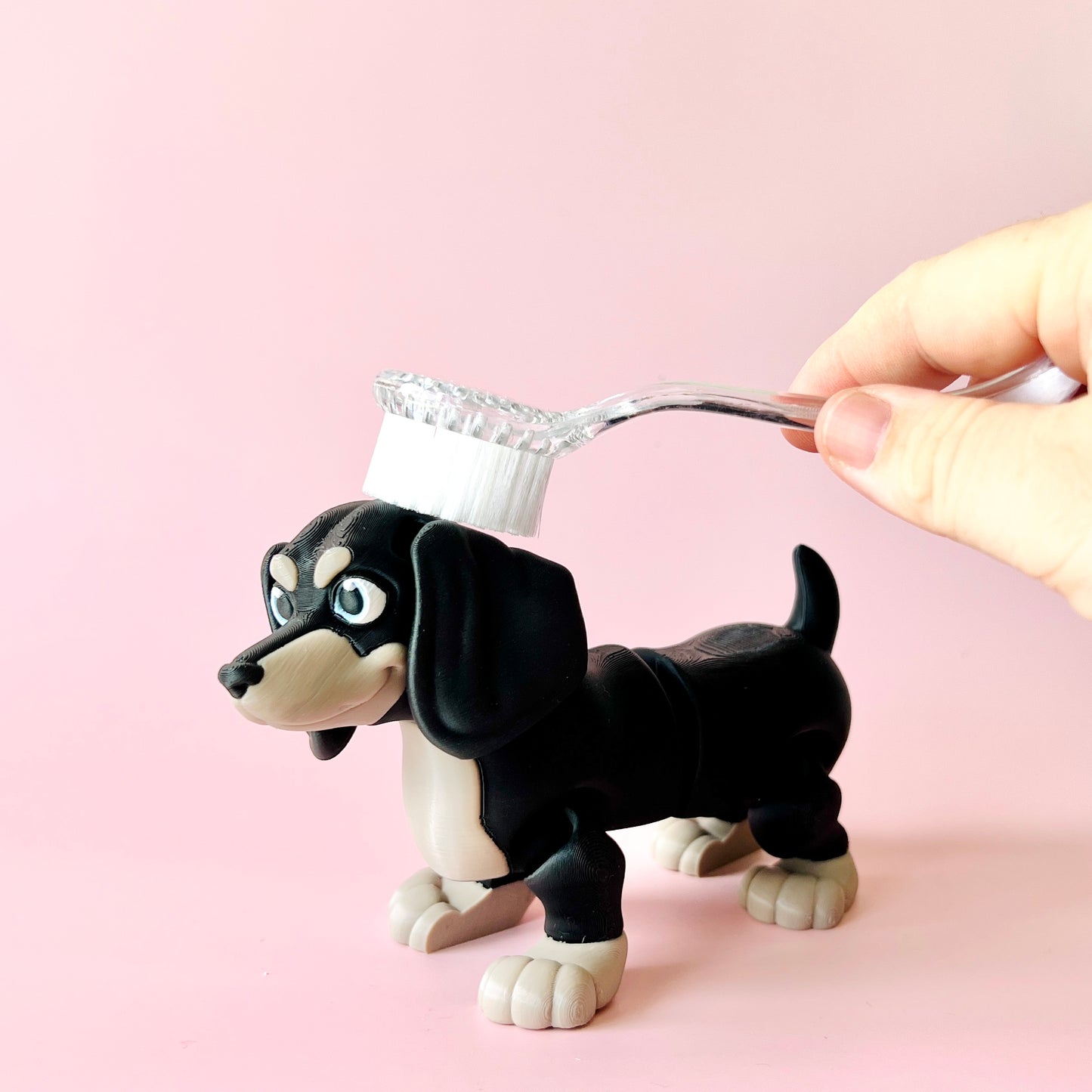 A playful black and tan dog figurine with a toothbrush held above its head, set against a soft pink background.