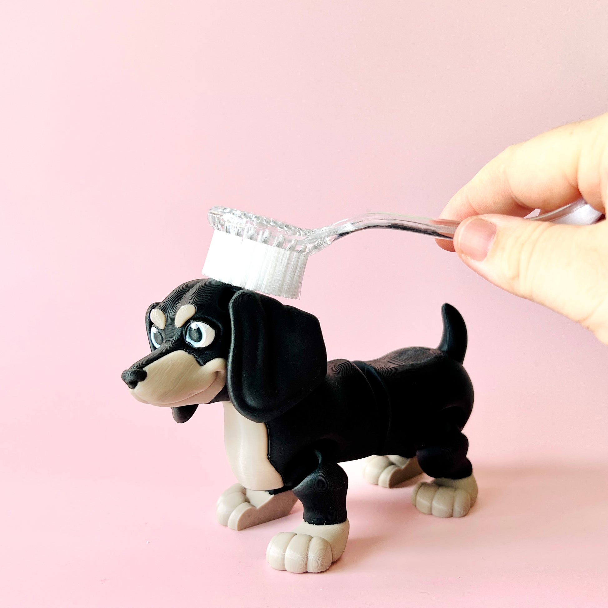 A playful black and tan dog figurine with a toothbrush held above its head, set against a soft pink background.