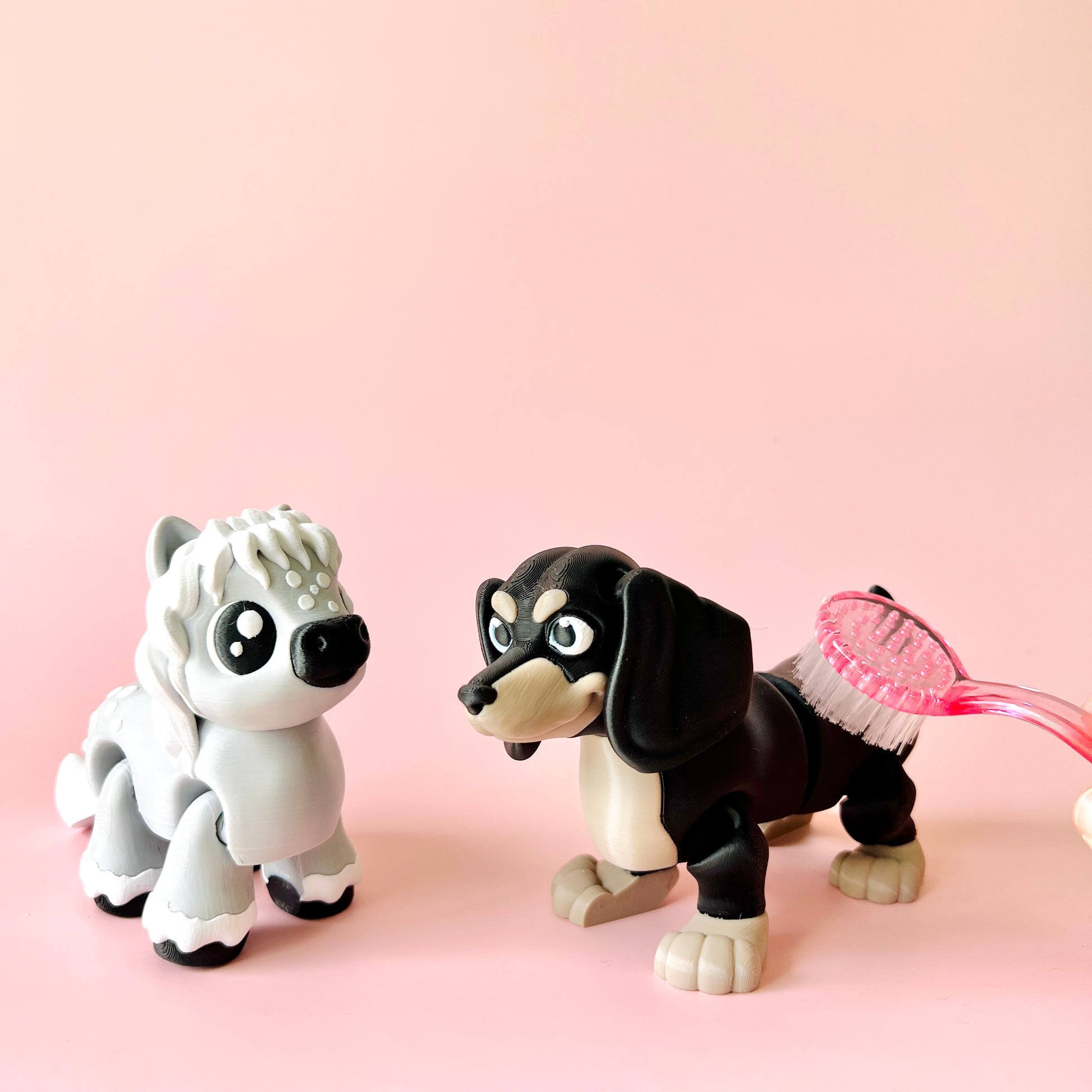 Two playful figurines of a fluffy white dog and a black dachshund with a pink brush against a soft pink background.