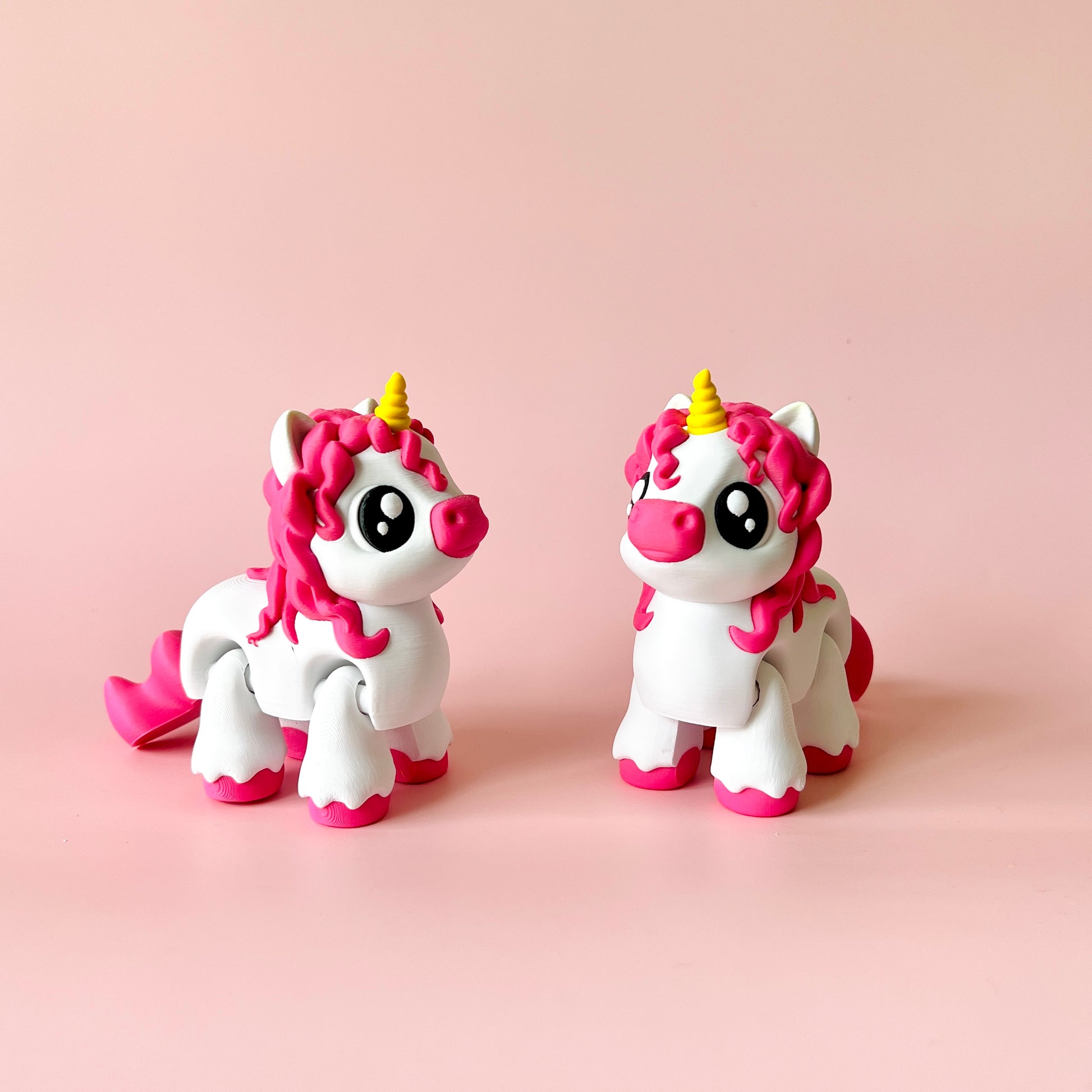 Two whimsical unicorn figures with pink manes and golden horns on a soft pink background.