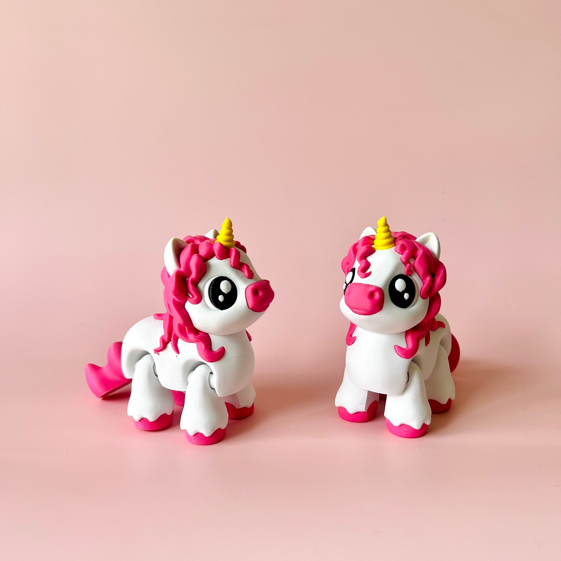 Two whimsical unicorn figures with pink manes and bright eyes against a soft pink background.