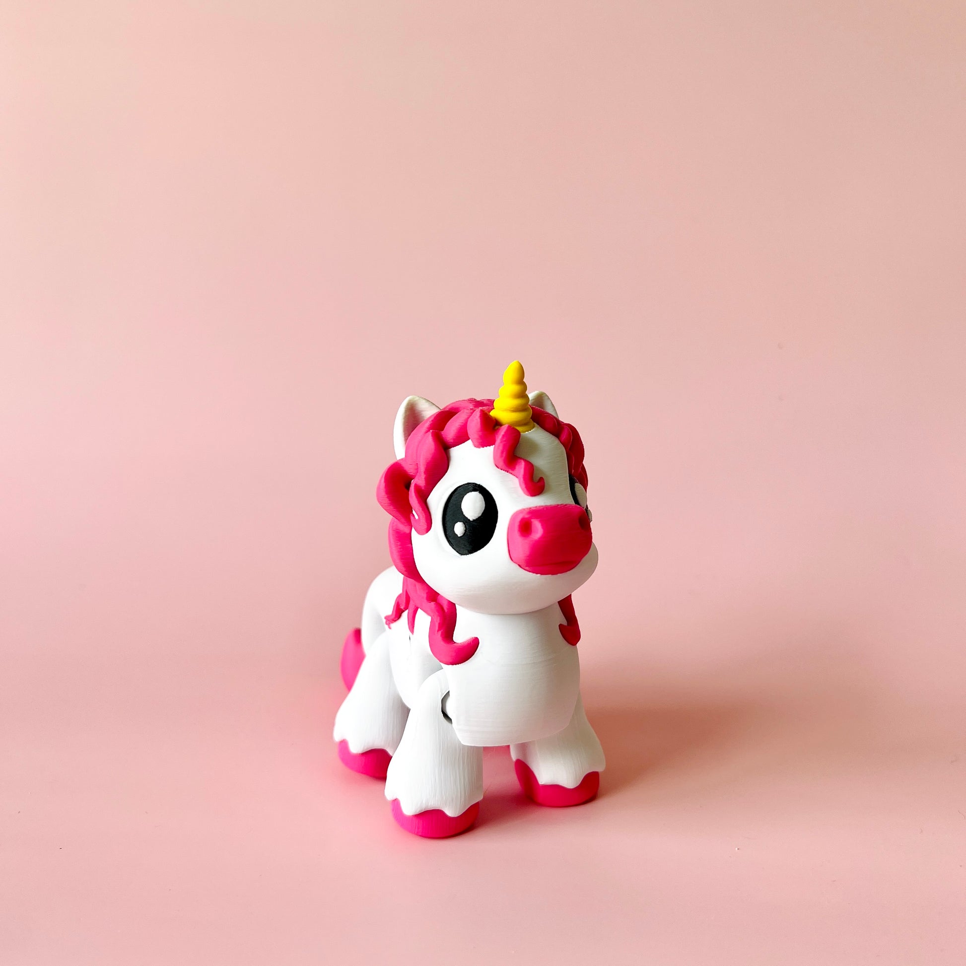 A whimsical unicorn figure with pink mane and a golden horn stands against a soft pink background.