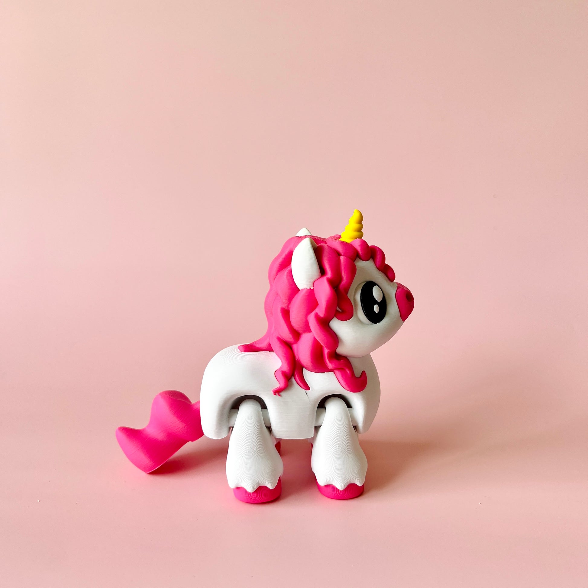 A whimsical unicorn figure with pink curls and a golden horn against a soft pink background.