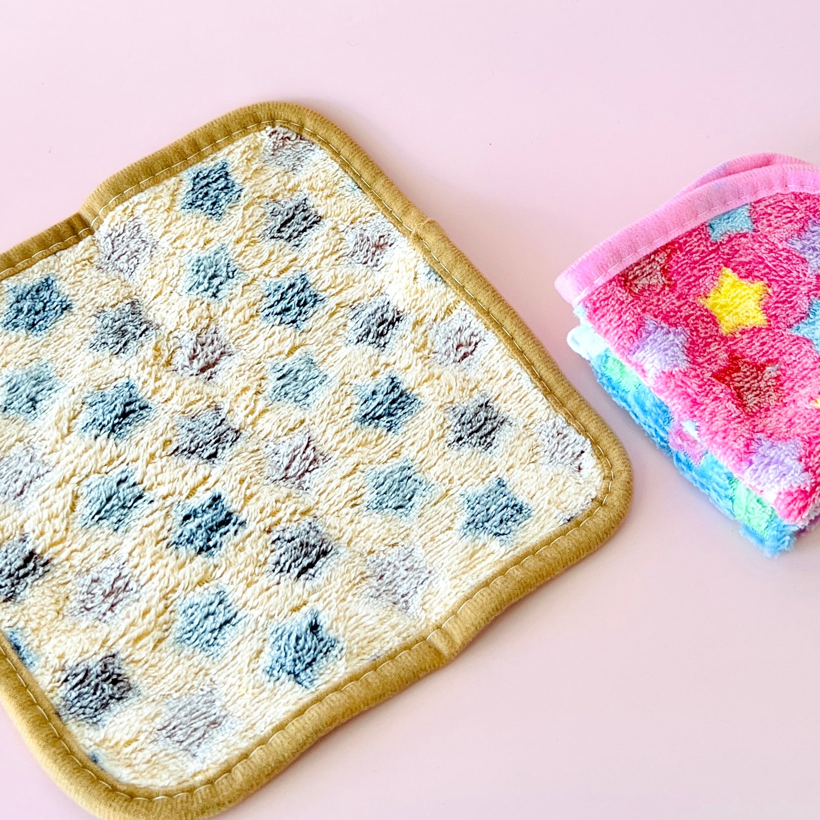 Colorful cloths with star patterns, one folded in pink and blue, next to a textured yellow and blue square on a pale backgrou