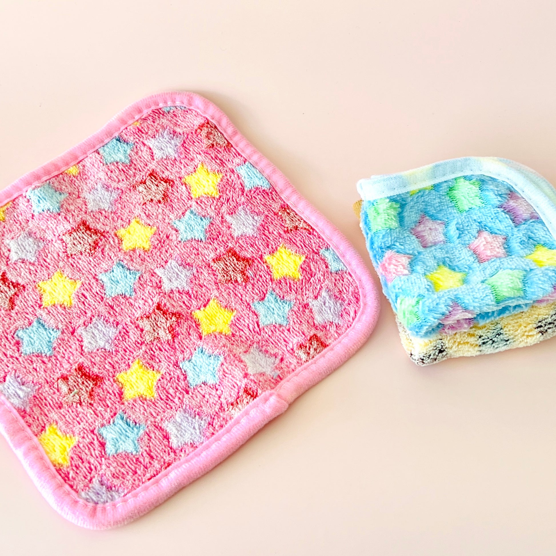 Two colorful cloths with star patterns, one in pink with yellow and blue stars, the other in pastel hues.