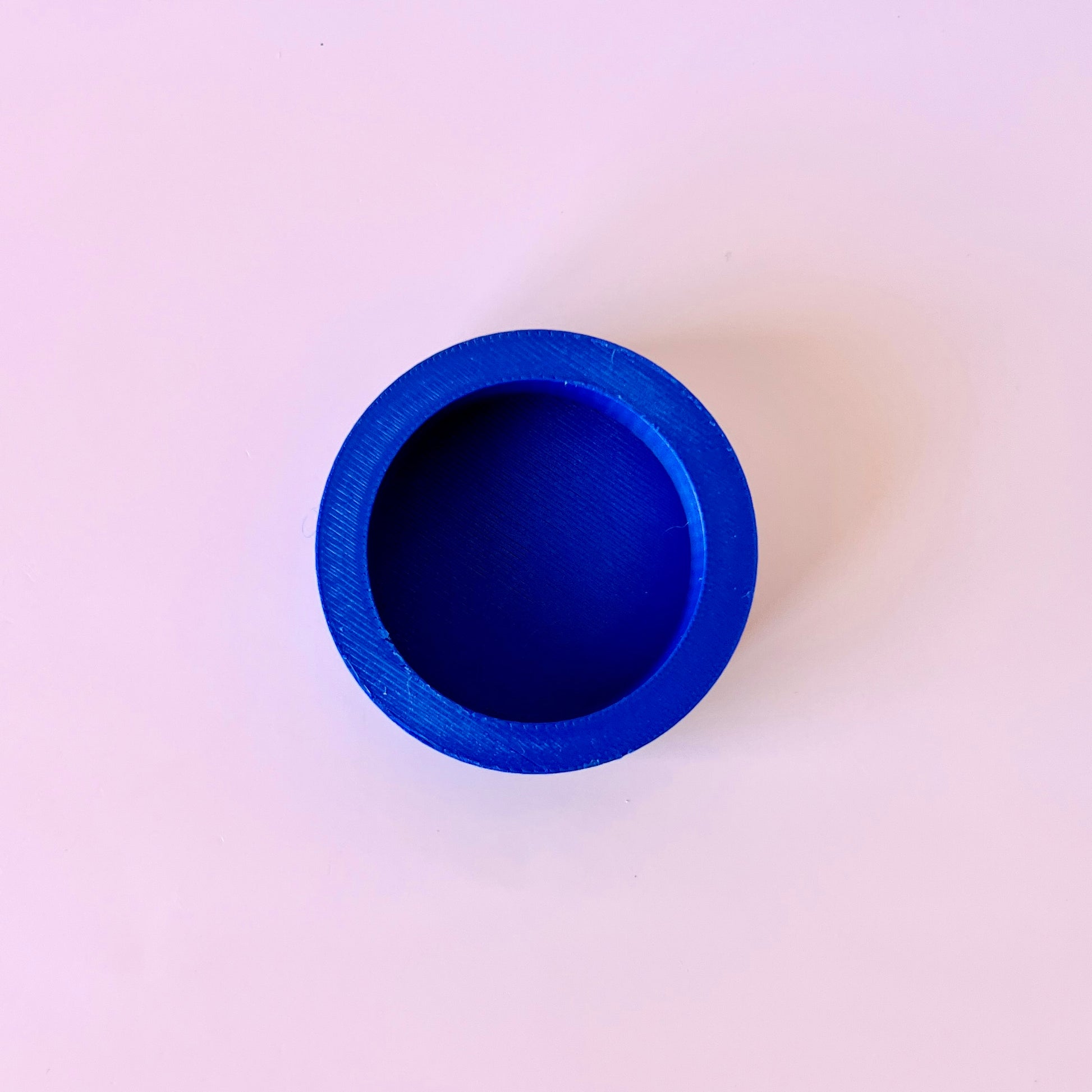 Bright blue circular shape with a smooth, matte finish, set against a soft pink background.