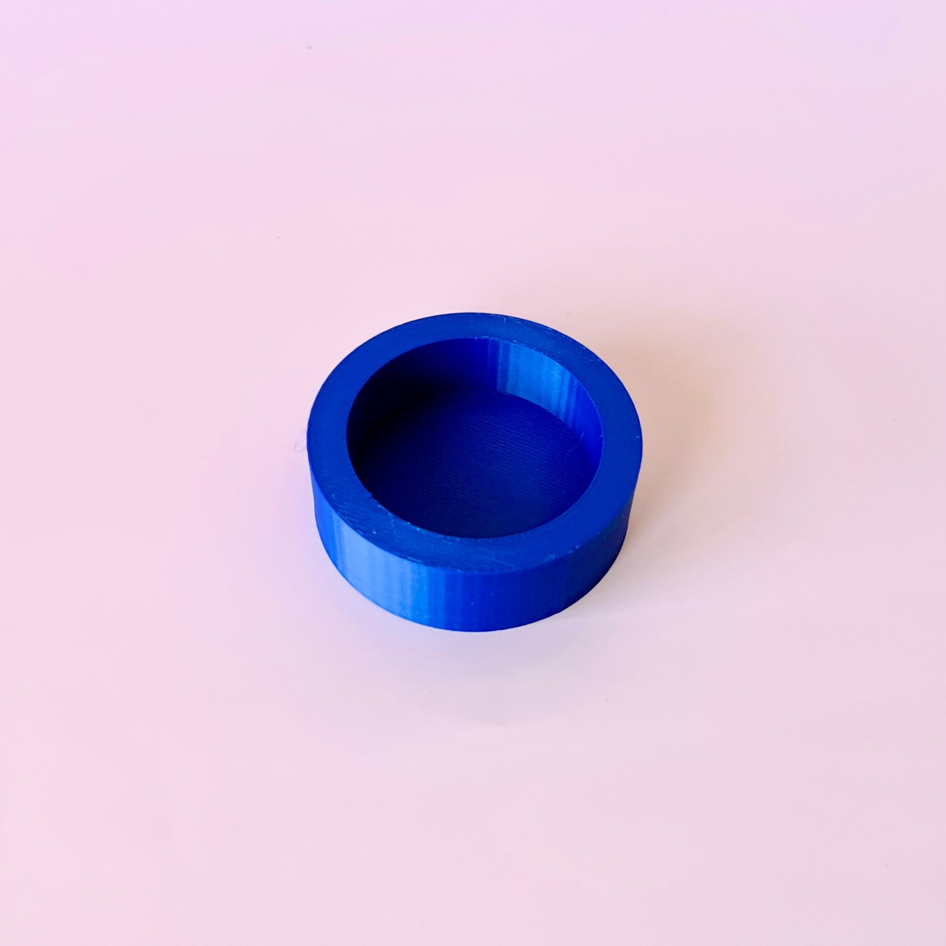 Bright blue circular shape with a smooth surface, placed on a soft pink background.