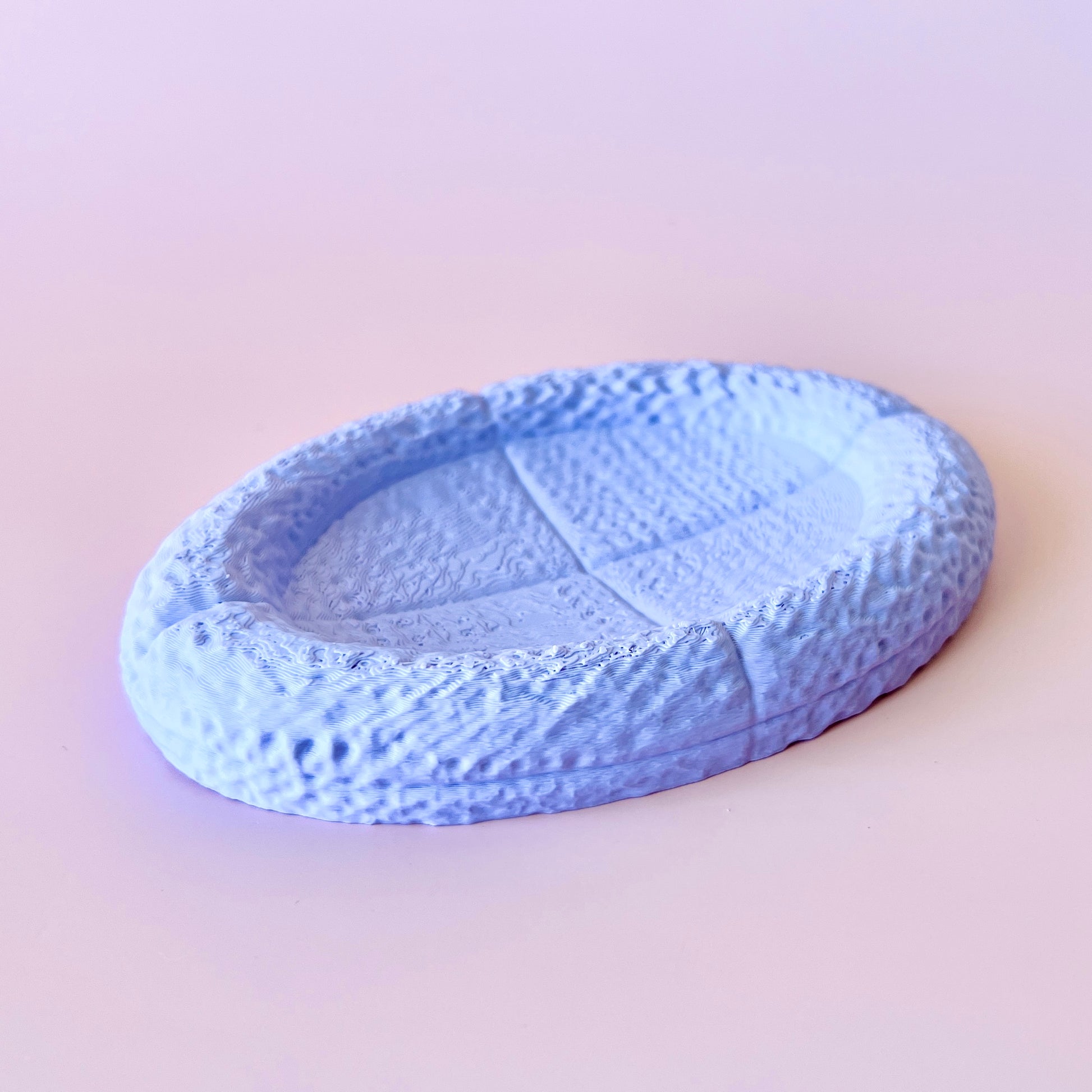 A textured, light blue oval dish with a raised edge, sitting against a soft pink background.