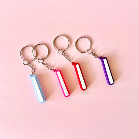 Four vibrant keychains in blue, pink, red, and purple hang against a soft pink background, showcasing playful charm.