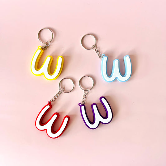 Four colorful keychains shaped like the letter "W" on a soft pink background.