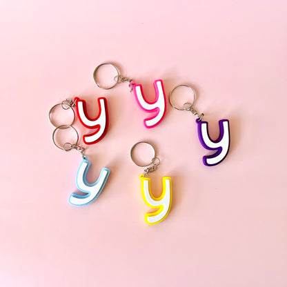 Colorful letter 'y' keychains in various hues arranged on a soft pink background.