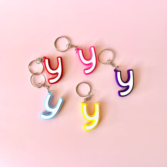 Colorful letter 'y' keychains in various hues arranged on a soft pink background.