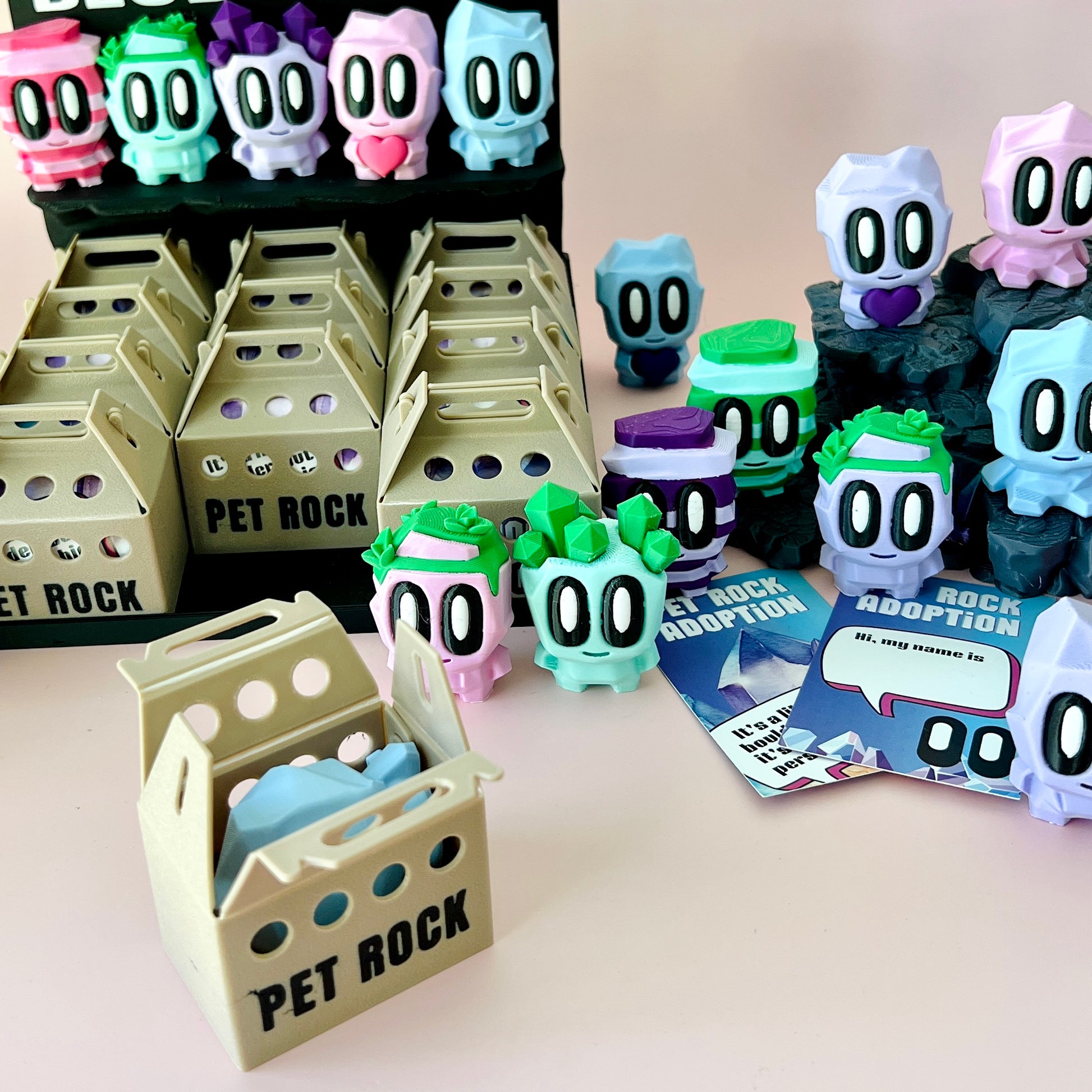 Colorful, cartoonish figures with large eyes and playful expressions, arranged alongside adoption cards and packaging.