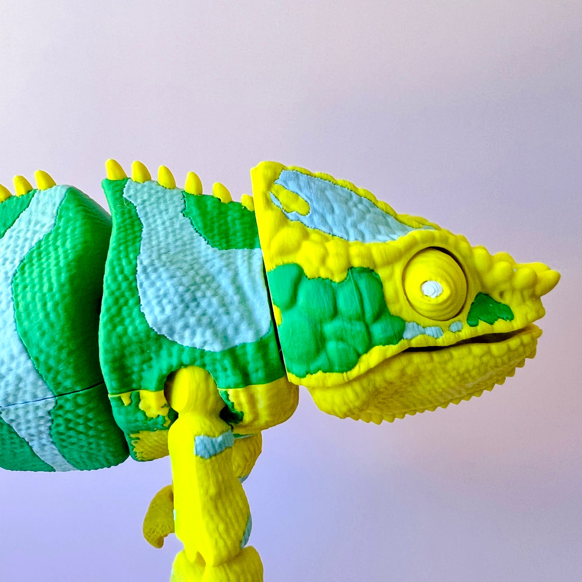 Colorful chameleon figure in vibrant green and yellow with textured skin and detailed features, set against a light backgroun
