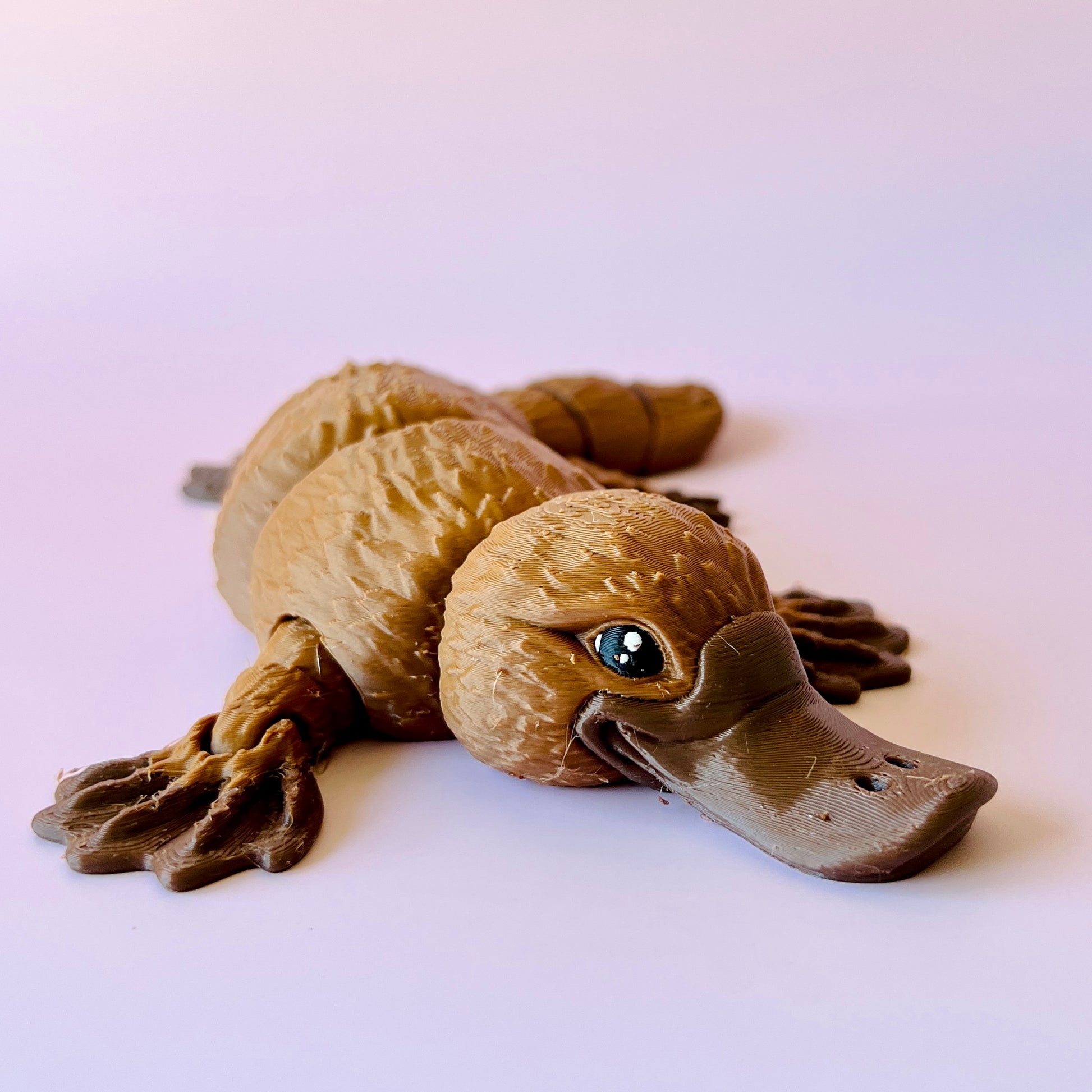 A detailed figurine of a platypus in shades of brown, featuring expressive eyes and textured body.