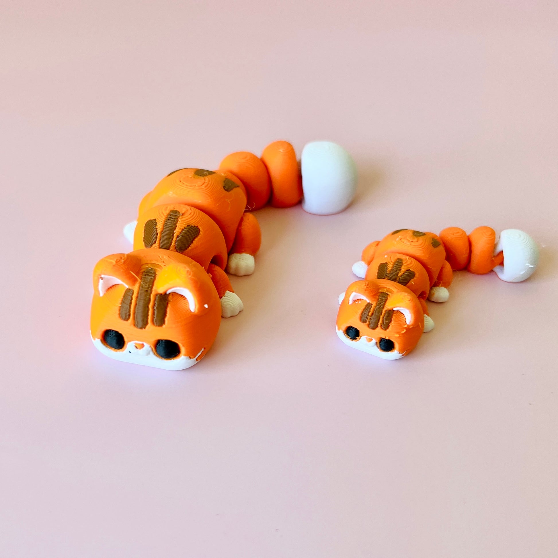 Two orange, segmented creatures with cat-like features, sitting on a soft pink background.