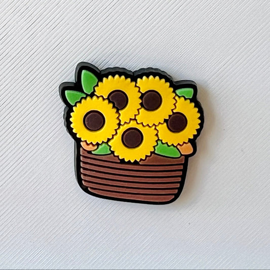 Bright yellow sunflowers in a brown basket, accented with green leaves against a textured white background.