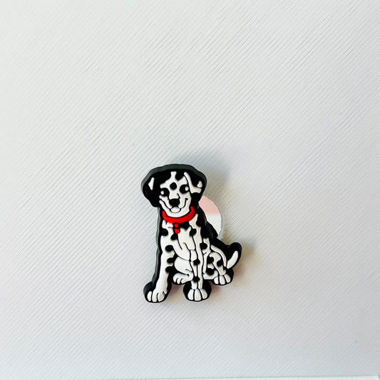 A playful black and white spotted dog sits, wearing a red collar, against a textured light background.