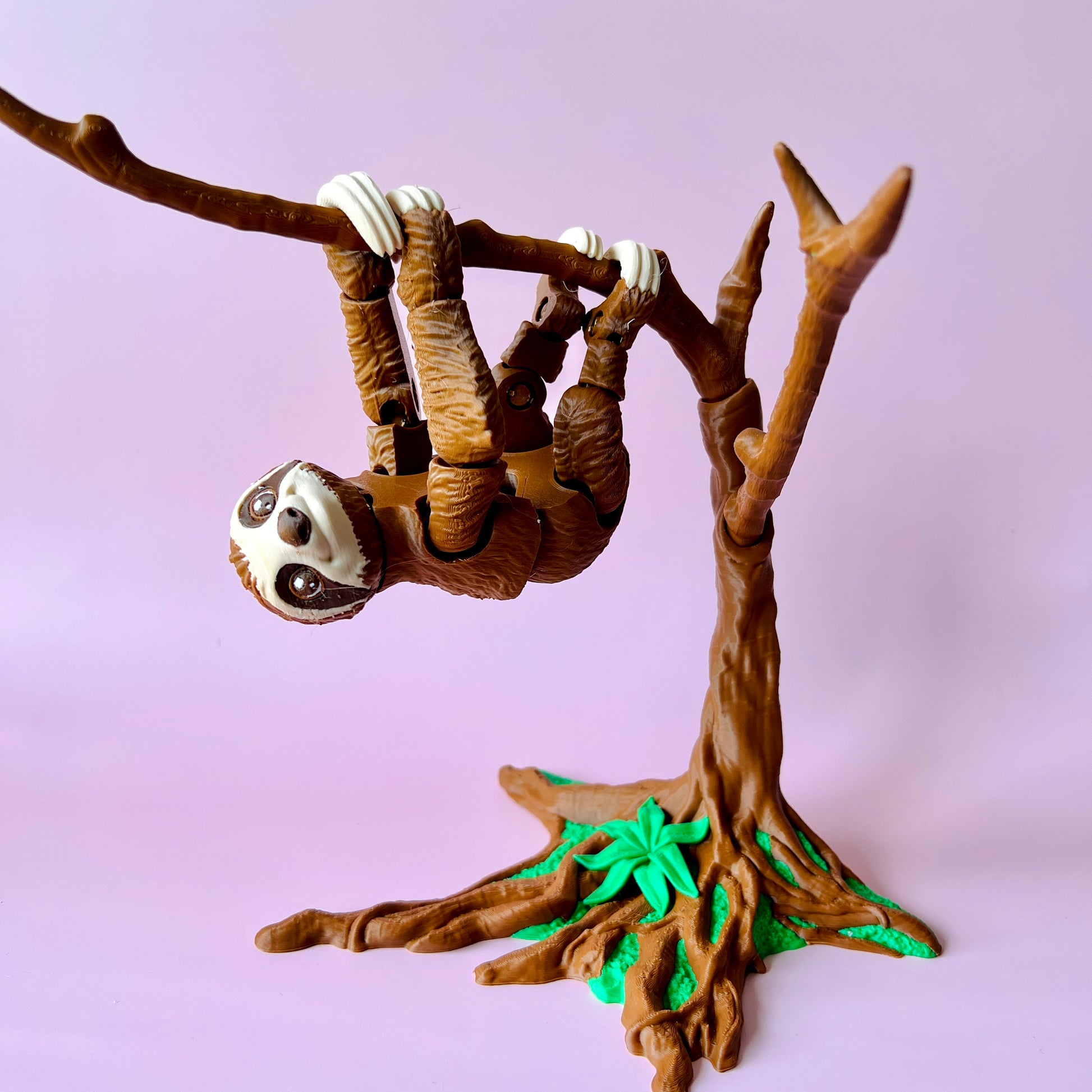 A playful sloth hangs upside down from a branch, surrounded by a tree and vibrant green leaves against a soft pink background