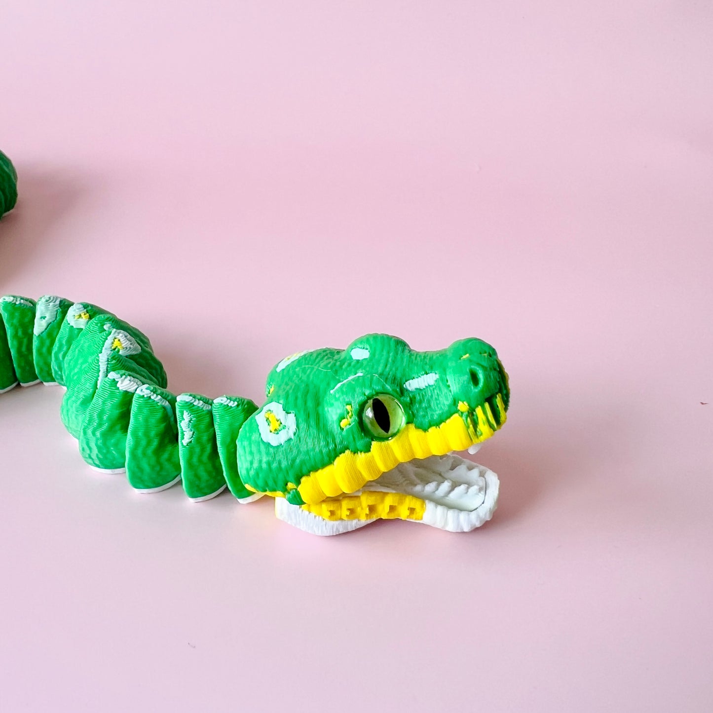Bright green serpent with a yellow underbelly and decorative white flowers on a soft pink background.