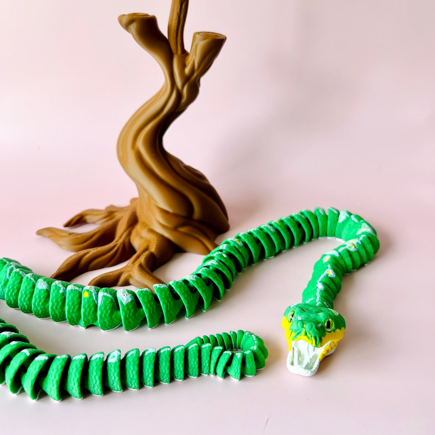 A vibrant green serpent curls around a stylized brown tree trunk against a soft pink background.
