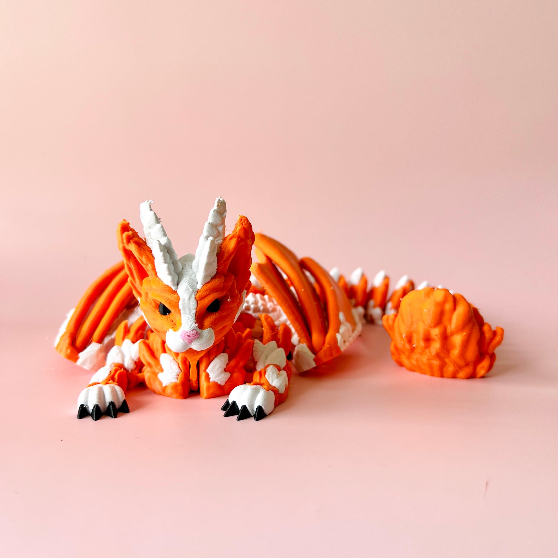An orange, stylized creature with white accents and sharp claws, resting on a soft pink background.