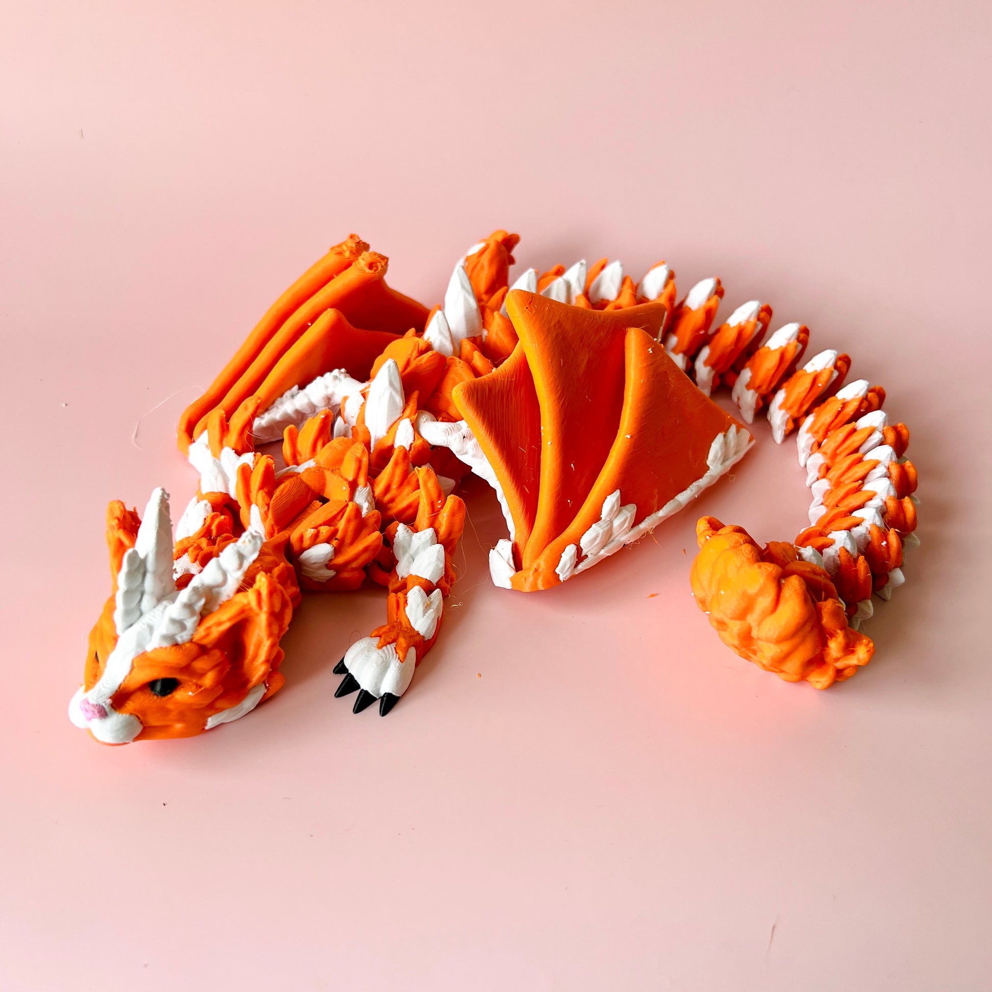 A vibrant orange dragon figure with white accents, featuring intricate details and a curled tail against a soft pink backgrou