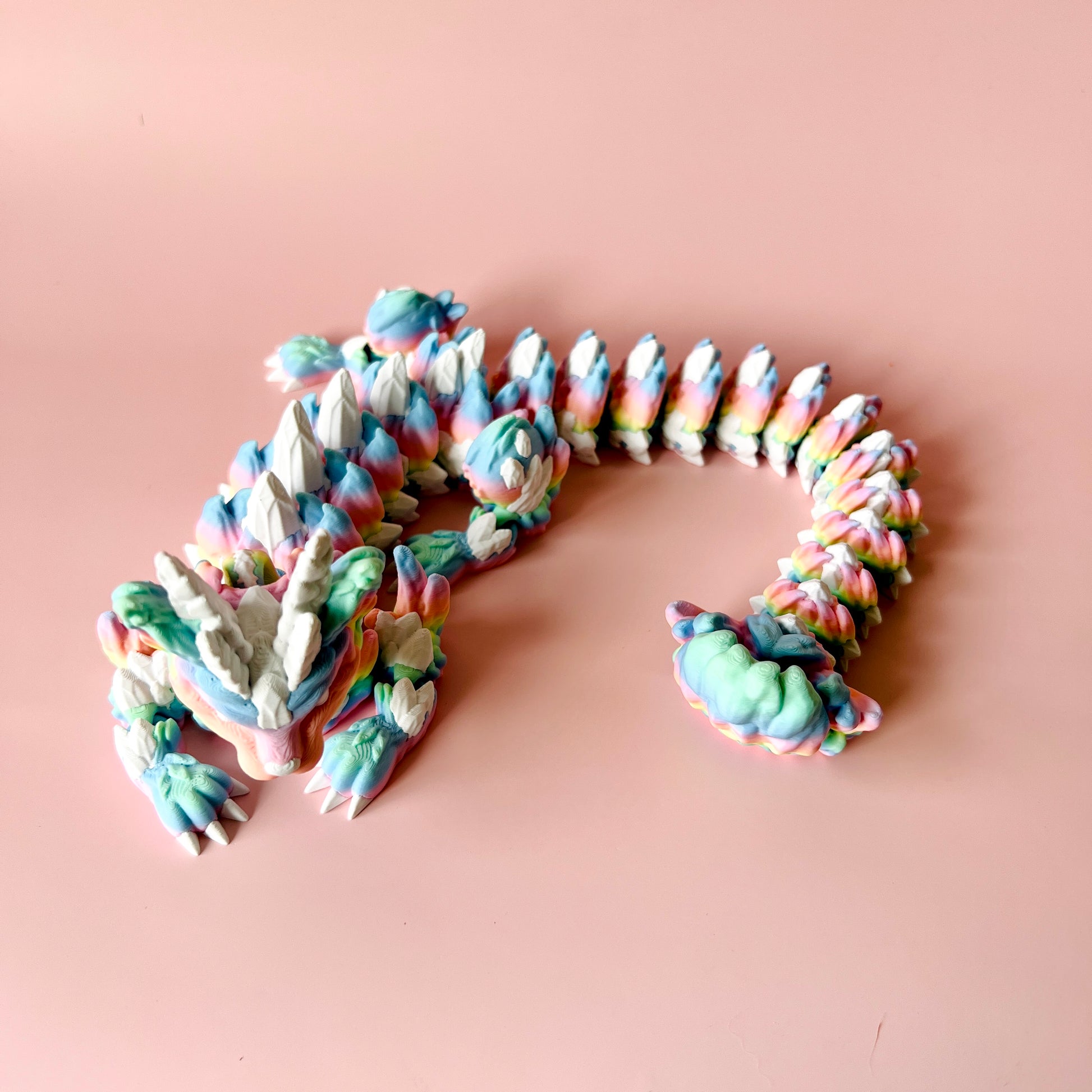 Colorful, textured creature with intricate scales and claws, resting on a soft pink background.