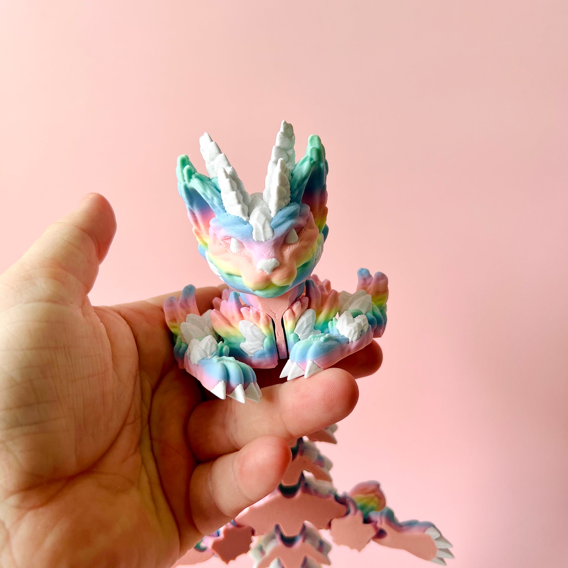 A colorful, whimsical creature with horns and claws is held against a soft pink background.