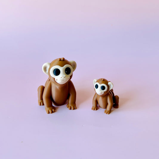 Two cute, cartoonish brown monkeys with large eyes sit on a soft pink background, one larger than the other.