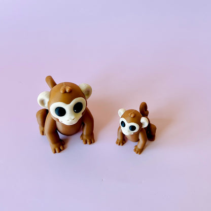 Two cute, brown monkey figures with large eyes, one smaller than the other, set against a soft pink background.